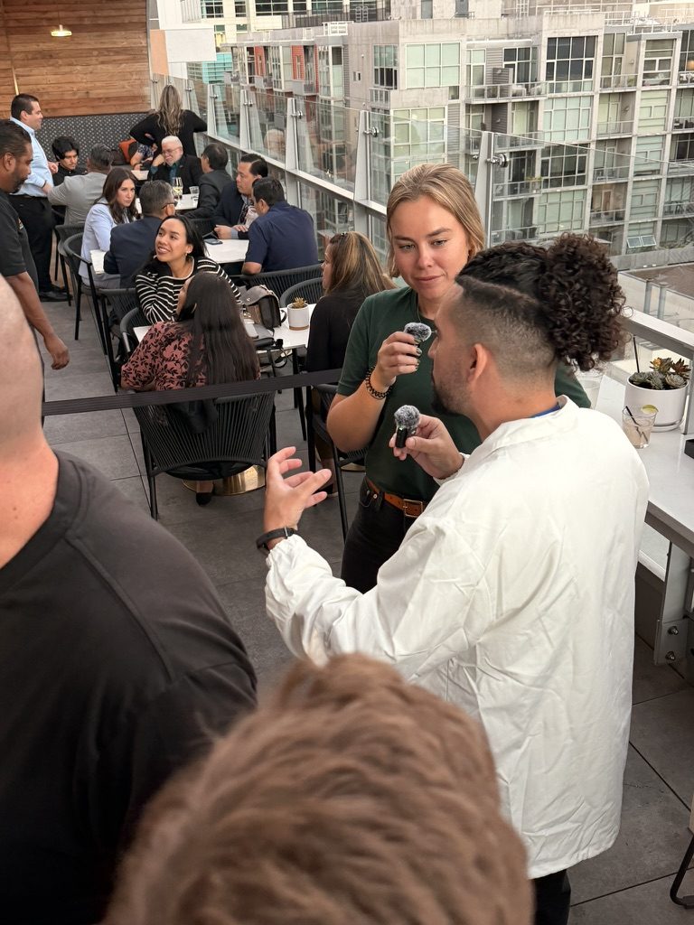 An attendee is interviewed on camera with handheld microphones during SERP & TURF, while brightonSEO San Diego attendees sit at tables along the rooftop railing